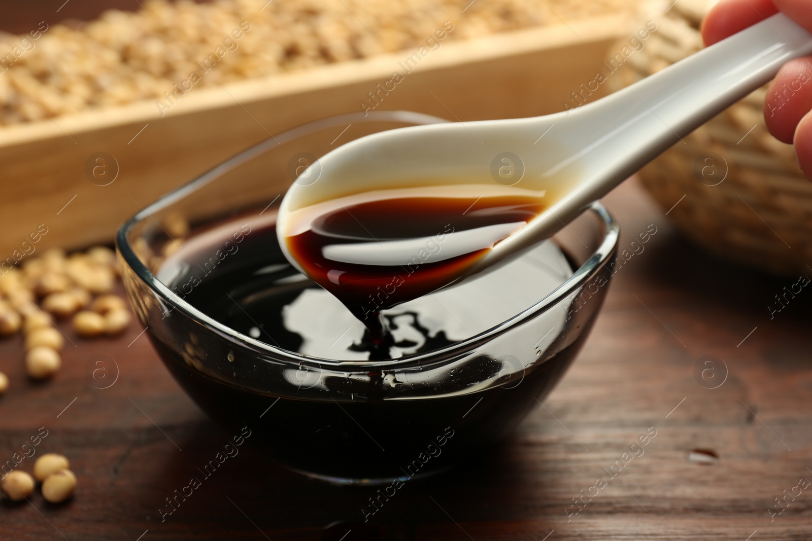 Photo of Taking soy sauce with spoon from bowl at wooden table, closeup