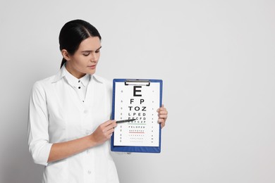 Ophthalmologist pointing at vision test chart on light background, space for text