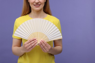 Woman with hand fan on violet background, closeup. Space for text