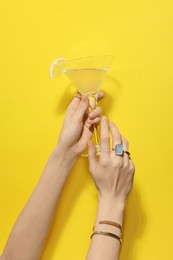 Photo of Woman holding martini glass of refreshing cocktail with lemon slice on yellow background, closeup
