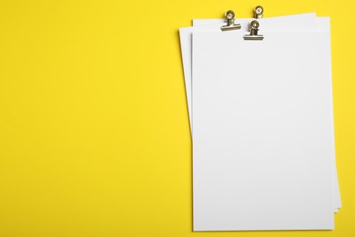 Photo of Sheets of paper with clips on yellow background, top view. Space for text