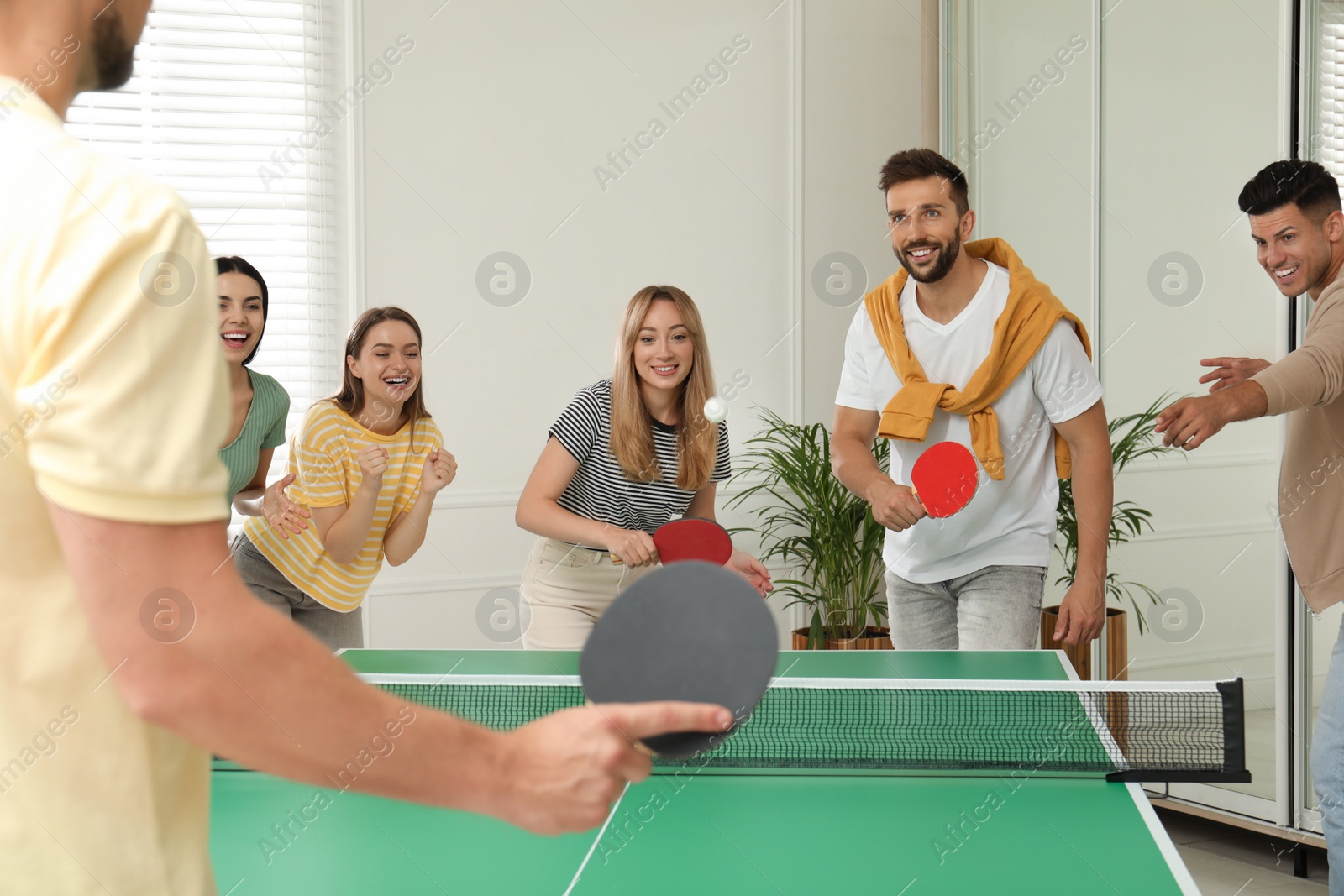 Photo of Happy friends playing ping pong together indoors