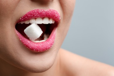 Woman with beautiful lips eating sugar cube on light grey background, closeup. Space for text