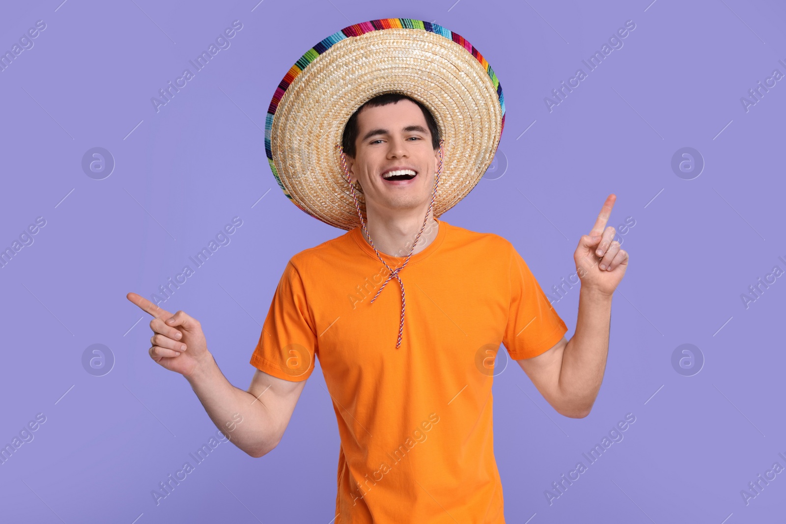 Photo of Young man in Mexican sombrero hat pointing at something on violet background