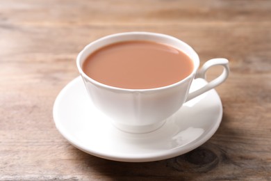 Delicious tea with milk in white cup on wooden table