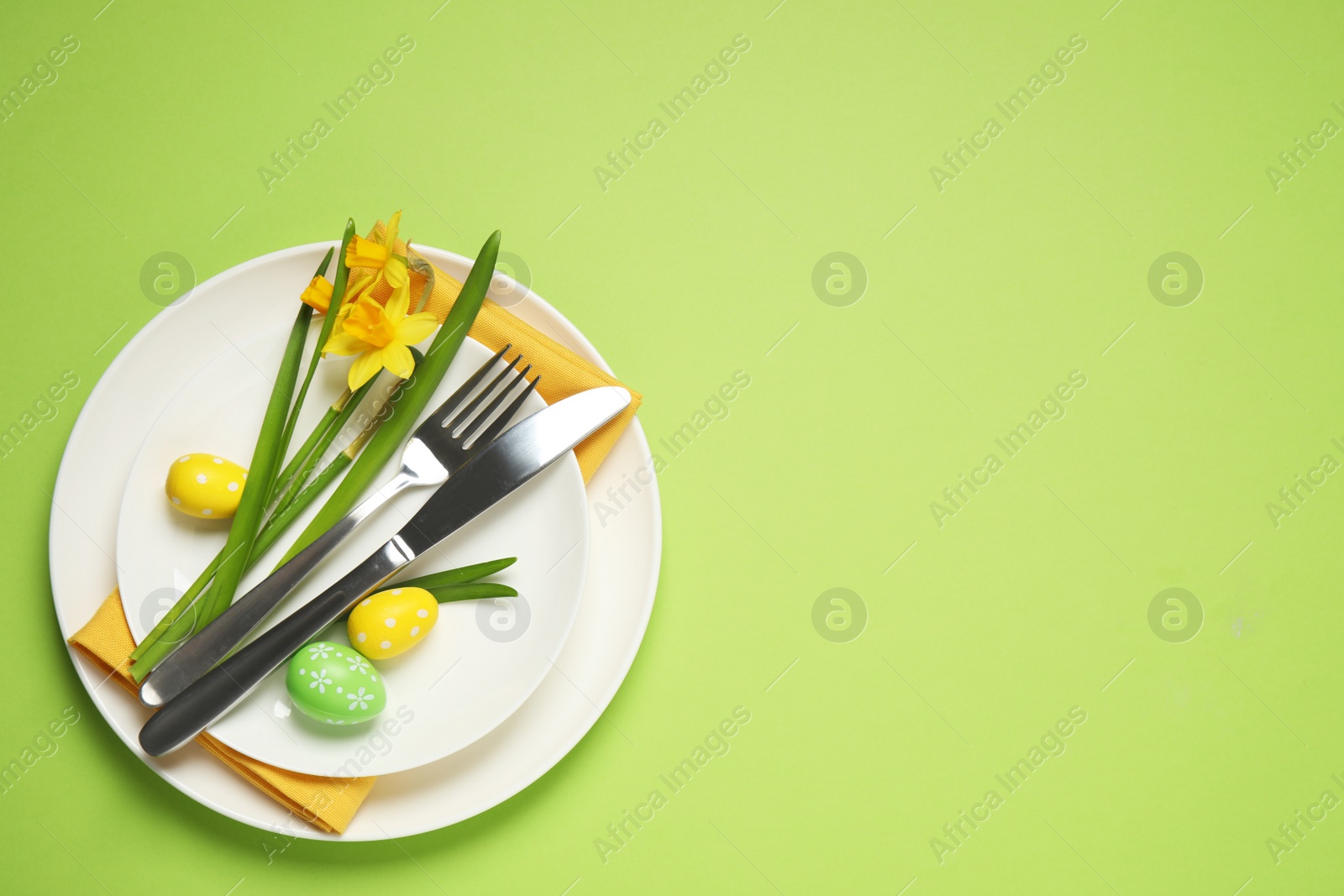 Photo of Festive Easter table setting with beautiful narcissuses and painted eggs, top view. Space for text