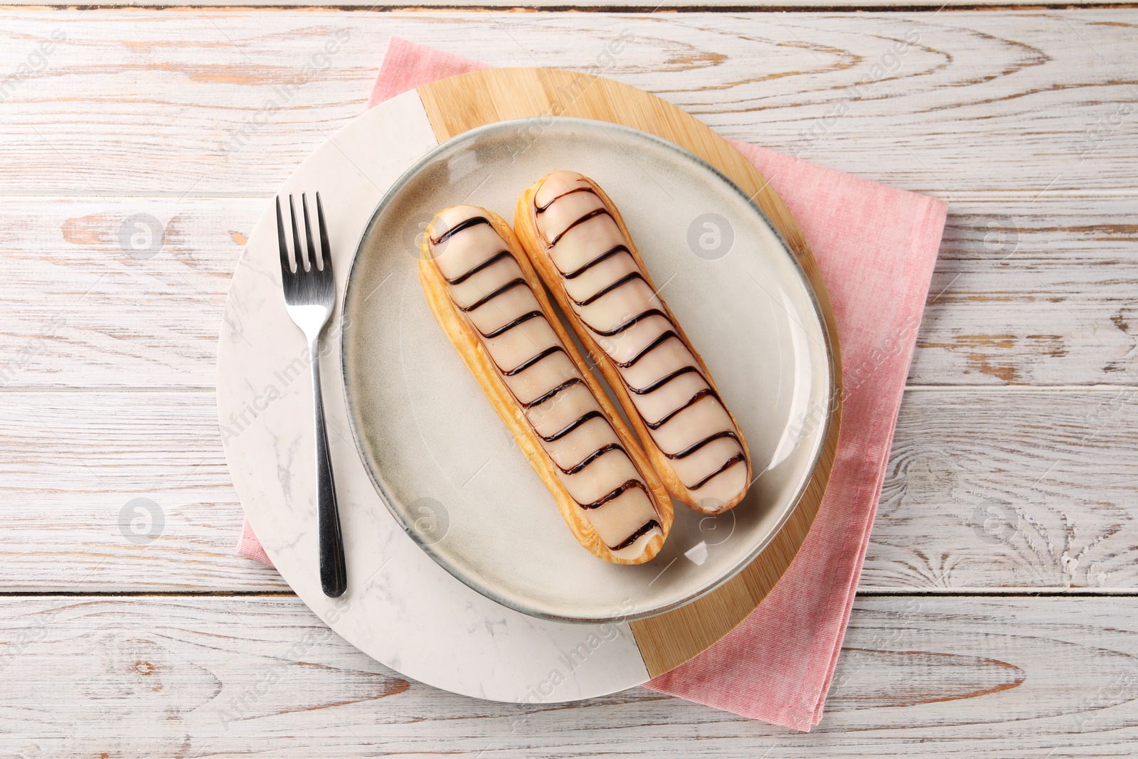 Photo of Tasty glazed eclairs served on wooden rustic table, top view