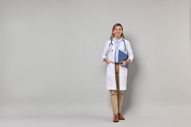 Portrait of happy doctor with stethoscope and clipboard on light grey background, space for text