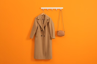 Photo of Hanger with beige coat and bag on orange wall