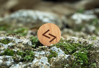 Photo of Wooden rune Jera on stone with moss outdoors, closeup