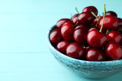Photo of Fresh ripe cherries in bowl on turquoise wooden table, closeup. Space for text