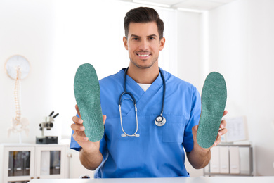 Handsome male orthopedist showing insoles in clinic