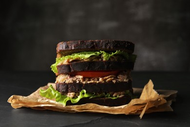 Delicious sandwich with tuna, tomatoes and lettuce on black table
