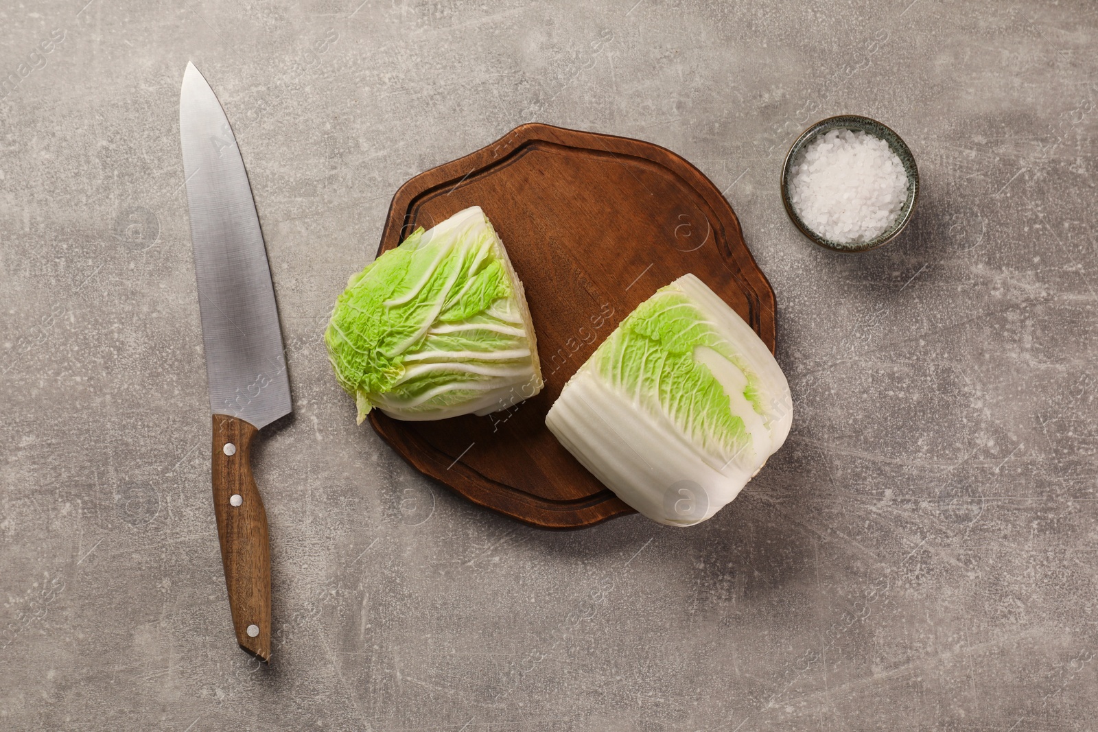 Photo of Halves of fresh Chinese cabbage, knife and salt on light grey table, flat lay