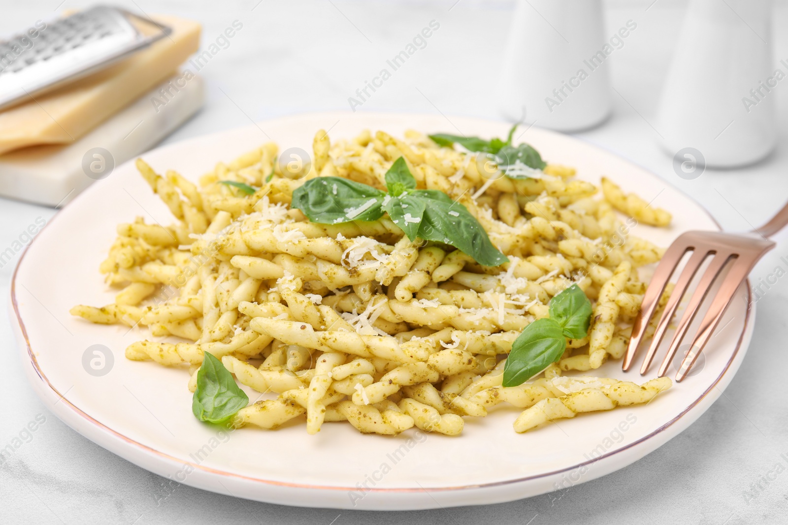 Photo of Plate of delicious trofie pasta with pesto sauce, cheese and basil leaves on white marble table