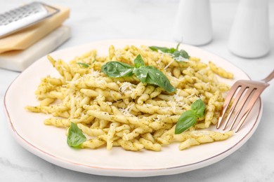 Plate of delicious trofie pasta with pesto sauce, cheese and basil leaves on white marble table