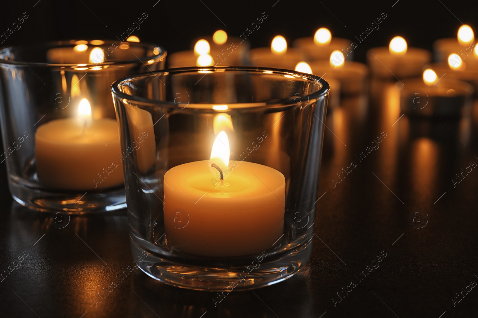 Photo of Wax candles burning on table in darkness, closeup