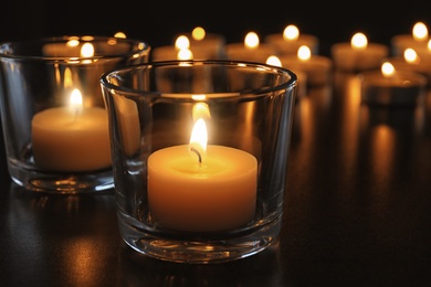 Photo of Wax candles burning on table in darkness, closeup