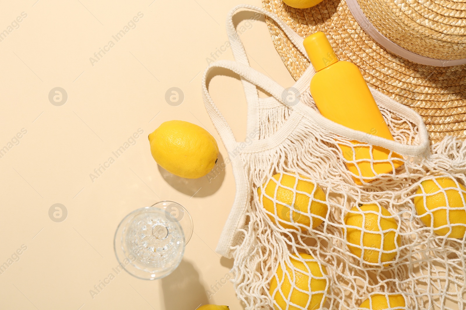 Photo of Fresh lemons, beach accessories in string bag and glass of drink on beige background, flat lay. Space for text