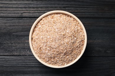 Photo of Bowl of wheat bran on black wooden table, top view