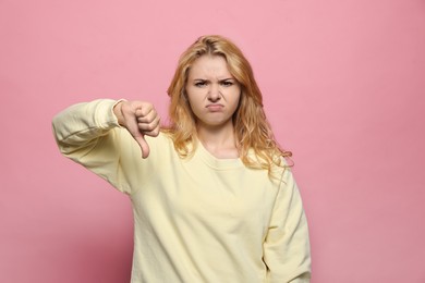 Dissatisfied young woman showing thumb down gesture on pink background