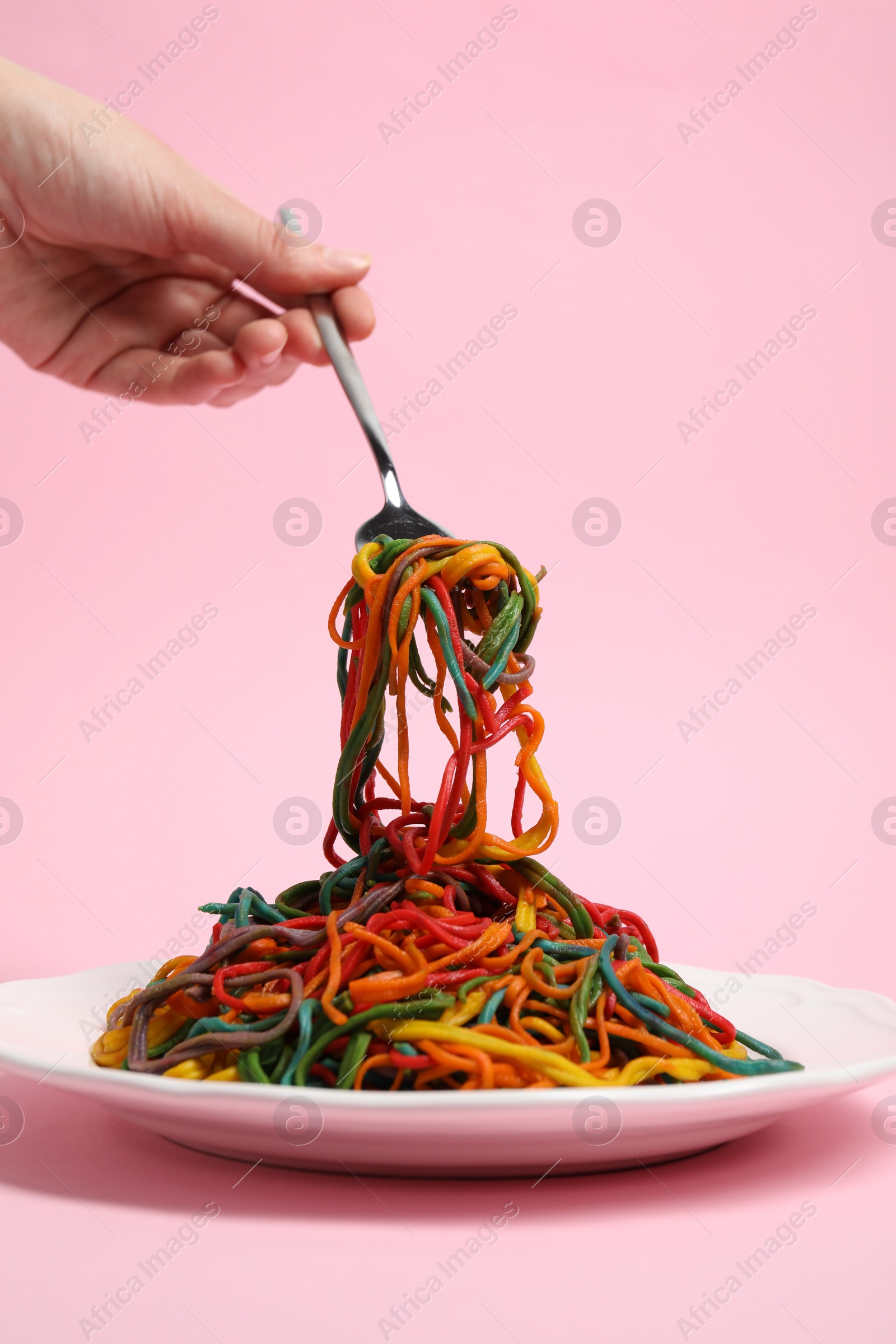 Photo of Woman eating delicious spaghetti painted with different food colorings on pink background, closeup