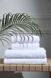 Photo of Stacked terry towels and green leaf on wicker bench indoors