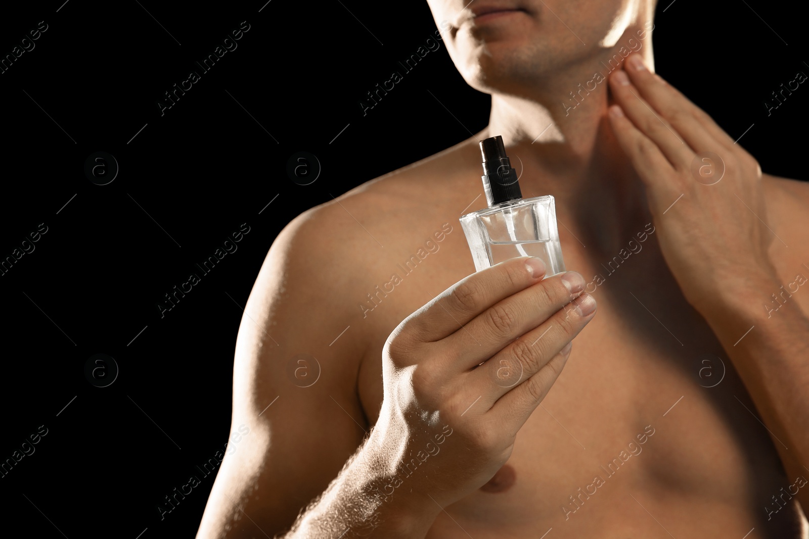Photo of Young man using perfume on black background, closeup