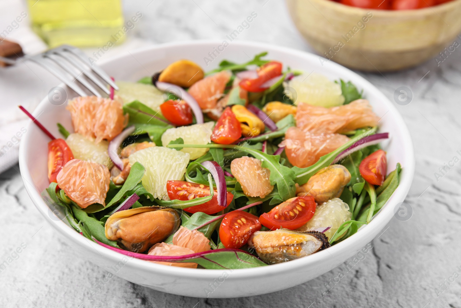 Photo of Delicious pomelo salad with tomatoes and mussels on white textured table, closeup