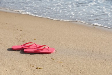 Photo of Stylish bright pink flip flops on sand near sea. Space for text