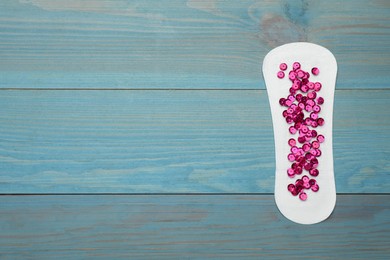 Photo of Sanitary pad with pink sequins on turquoise wooden background, top view and space for text. Menstrual cycle