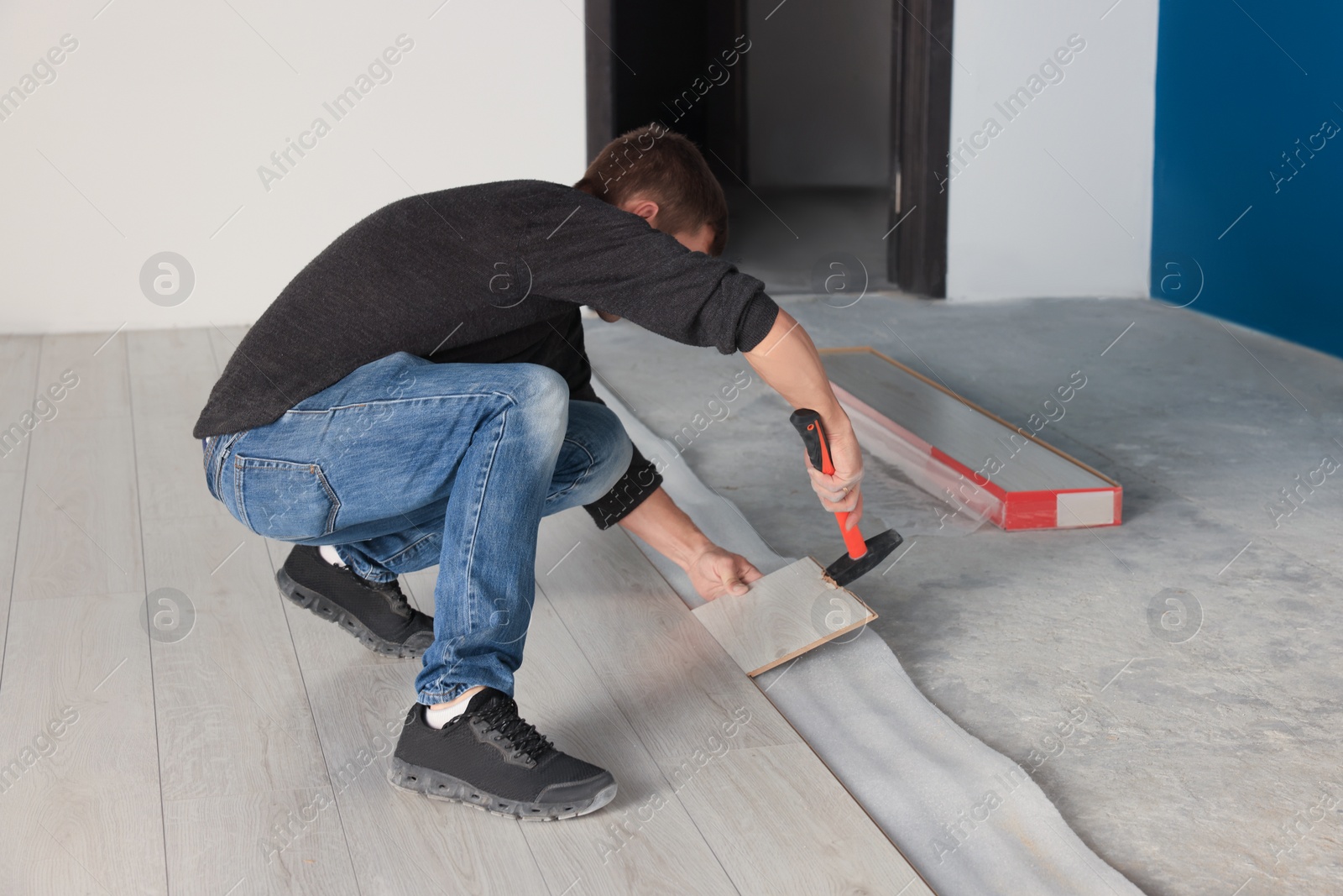 Photo of Professional worker using hammer during installation of new laminate flooring