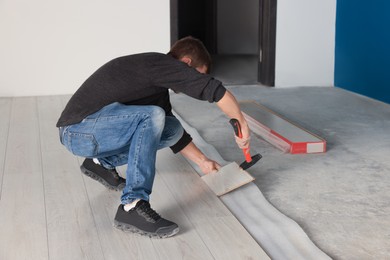 Photo of Professional worker using hammer during installation of new laminate flooring