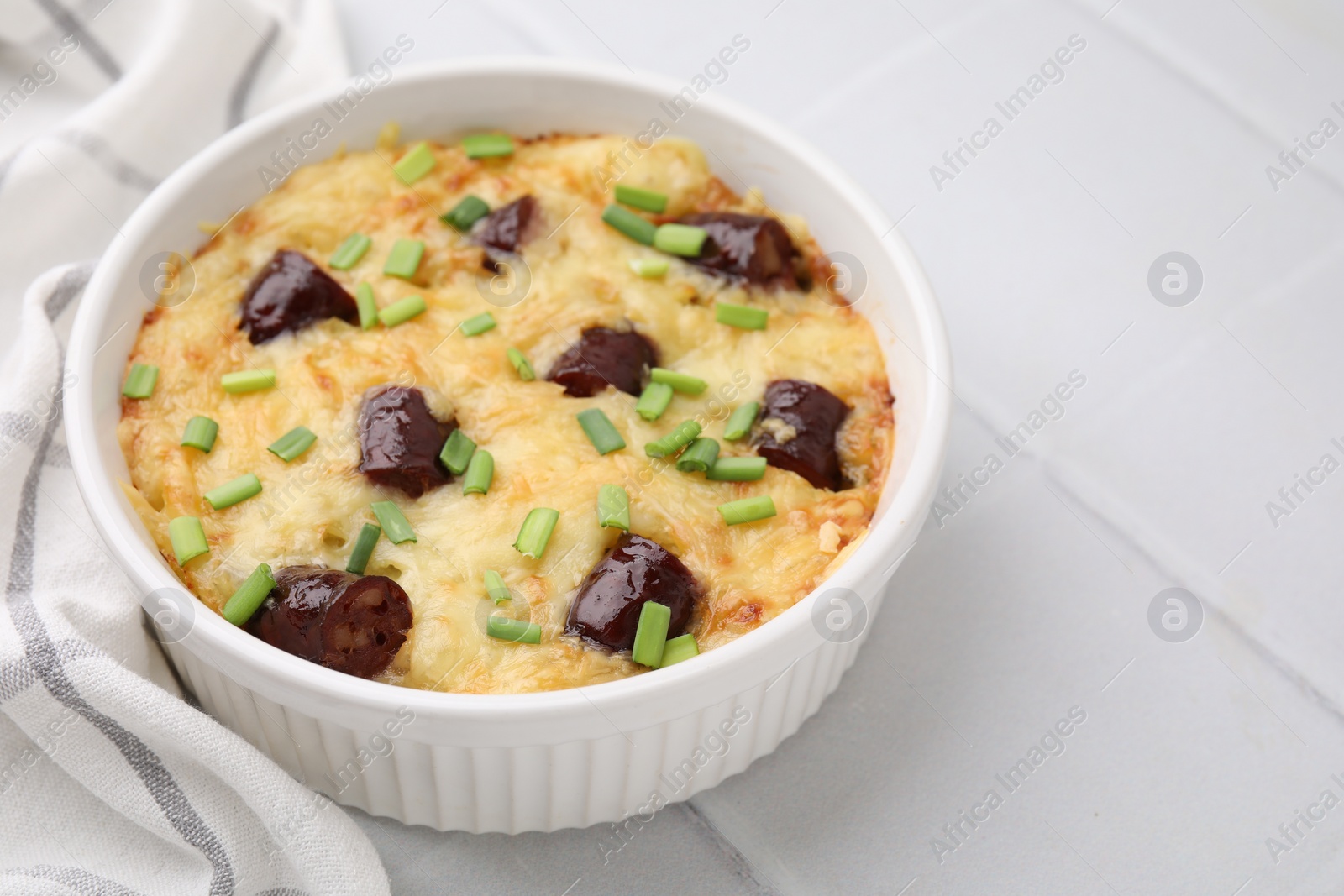 Photo of Tasty sausage casserole with green onions in baking dish on white tiled table, closeup