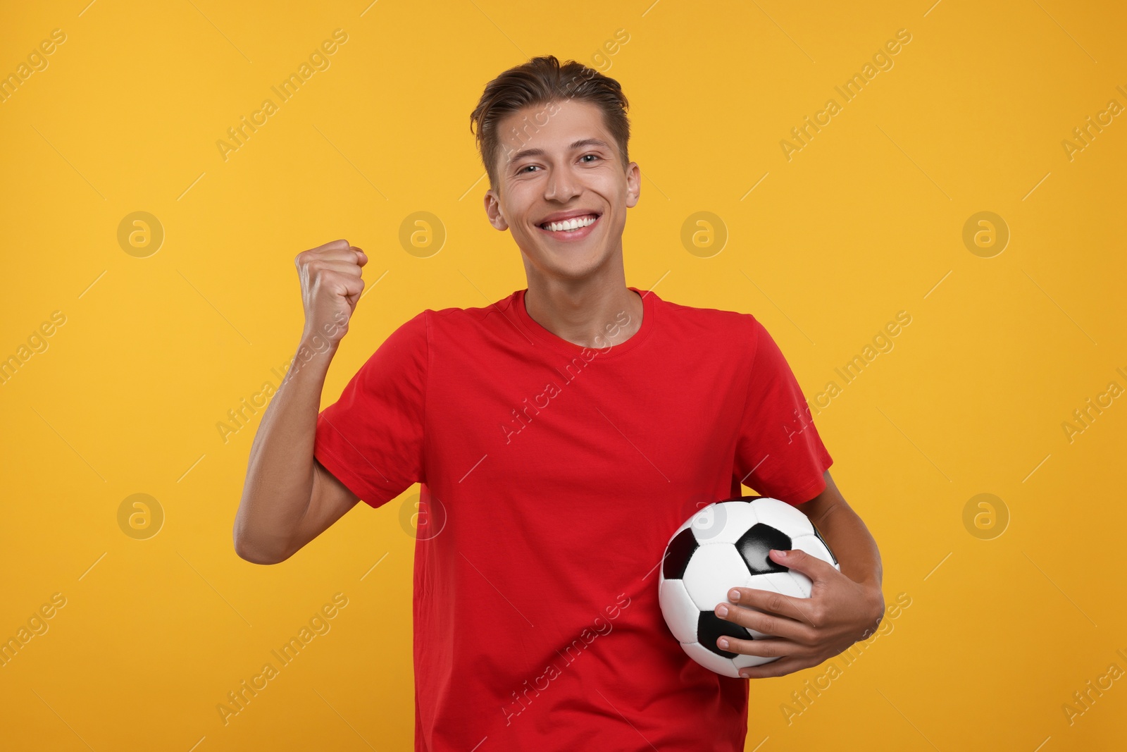 Photo of Happy sports fan with soccer ball celebrating on orange background