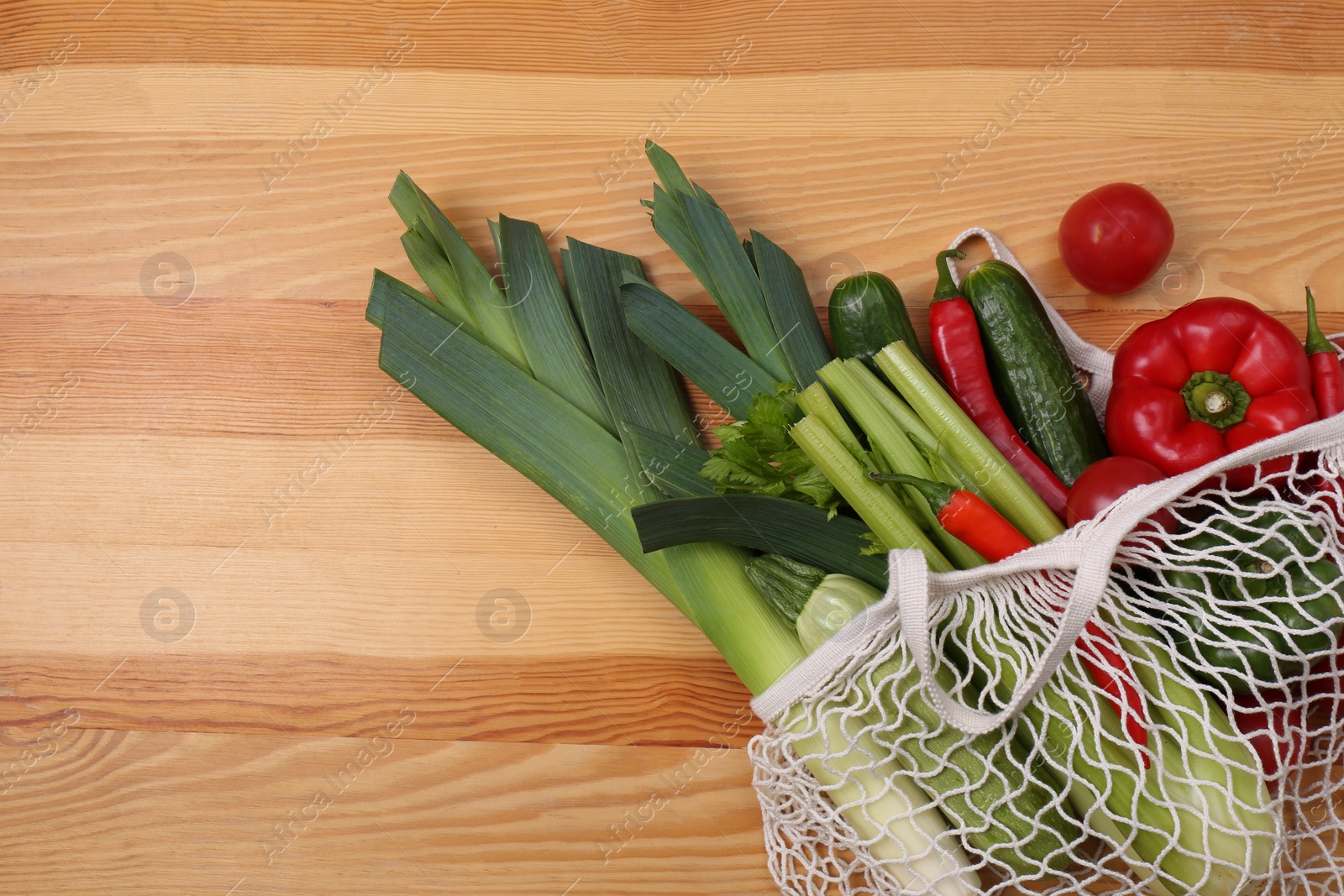 Photo of Net bag with vegetables on wooden background, top view