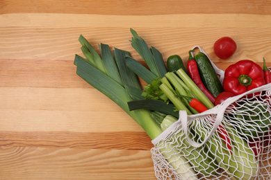 Photo of Net bag with vegetables on wooden background, top view