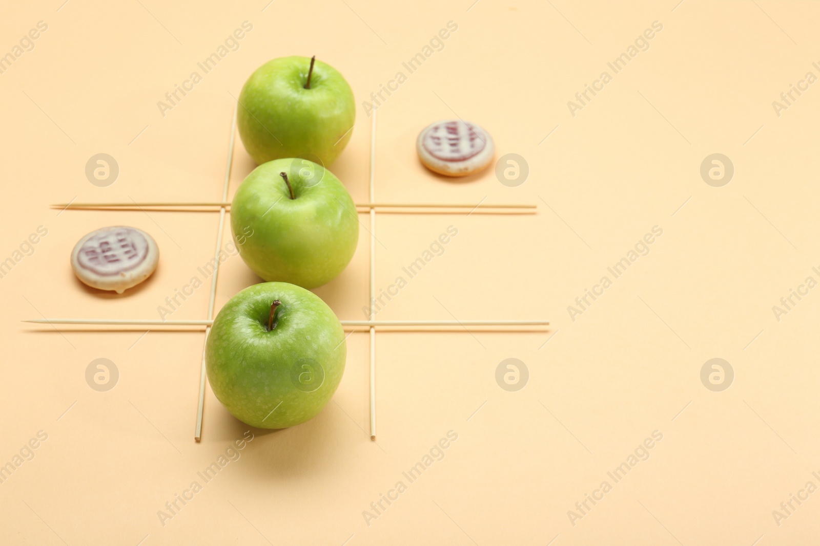 Photo of Tic tac toe game made with apples and cookies on beige background