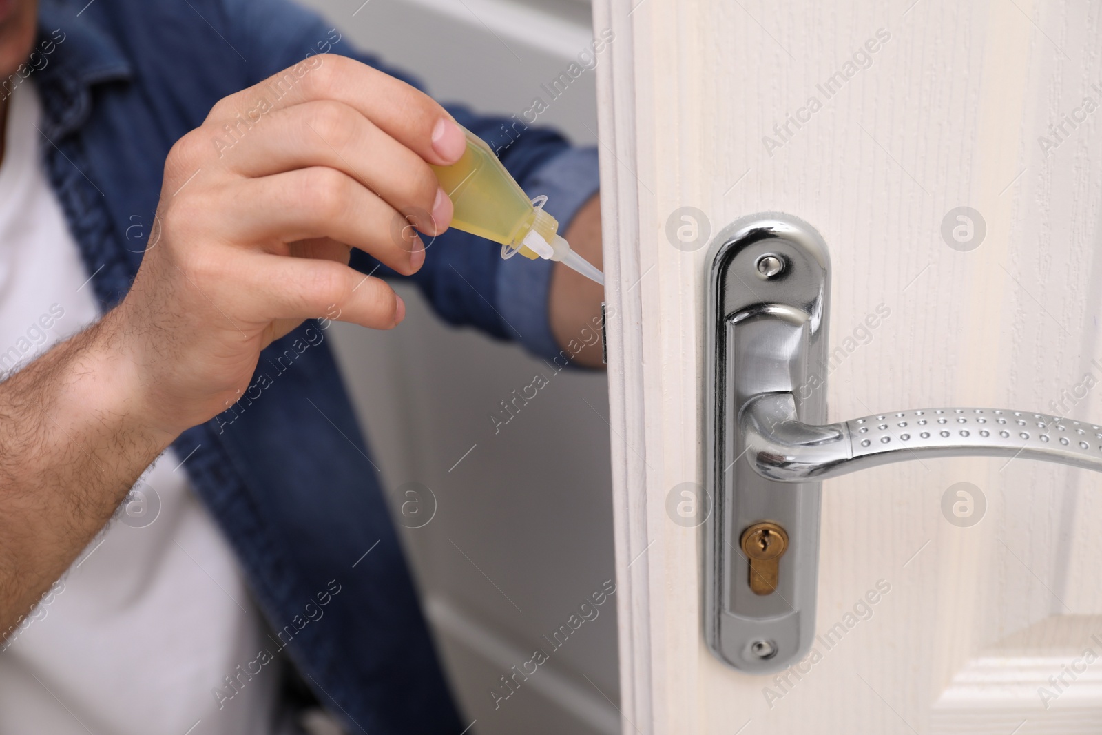 Photo of Repairman lubricating door lock at home, closeup