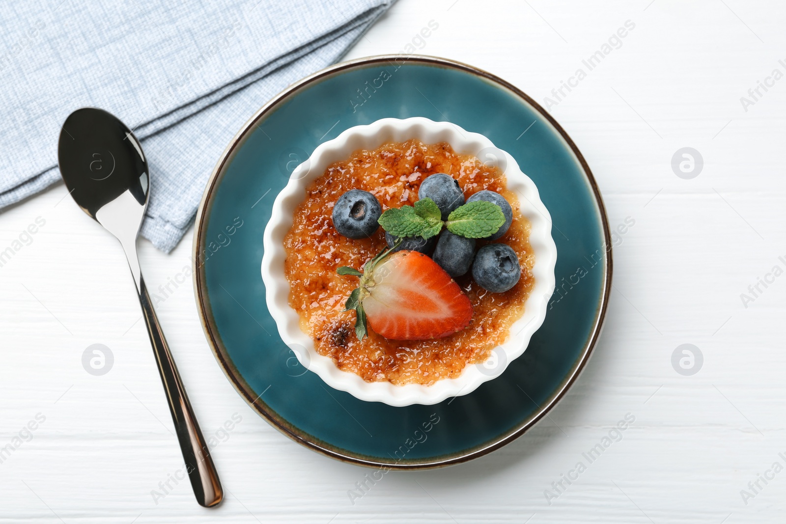 Photo of Delicious creme brulee with berries and mint in bowl on white wooden table, top view