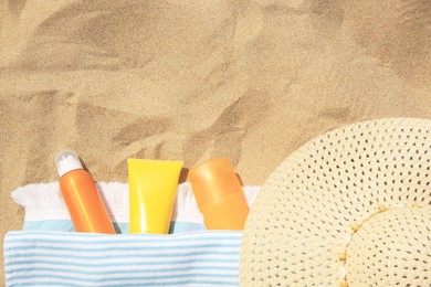 Sunscreens, hat and towel on sand, flat lay with space for text. Sun protection care