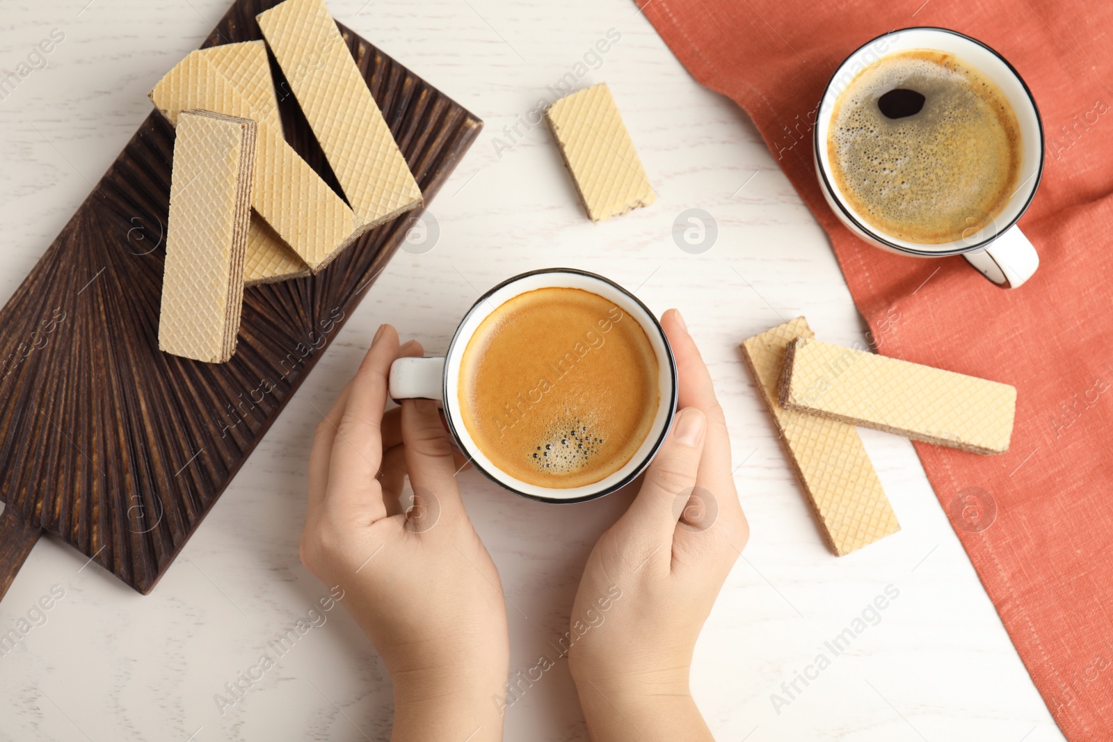 Photo of Woman having breakfast with delicious coffee and wafers at white wooden table, top view