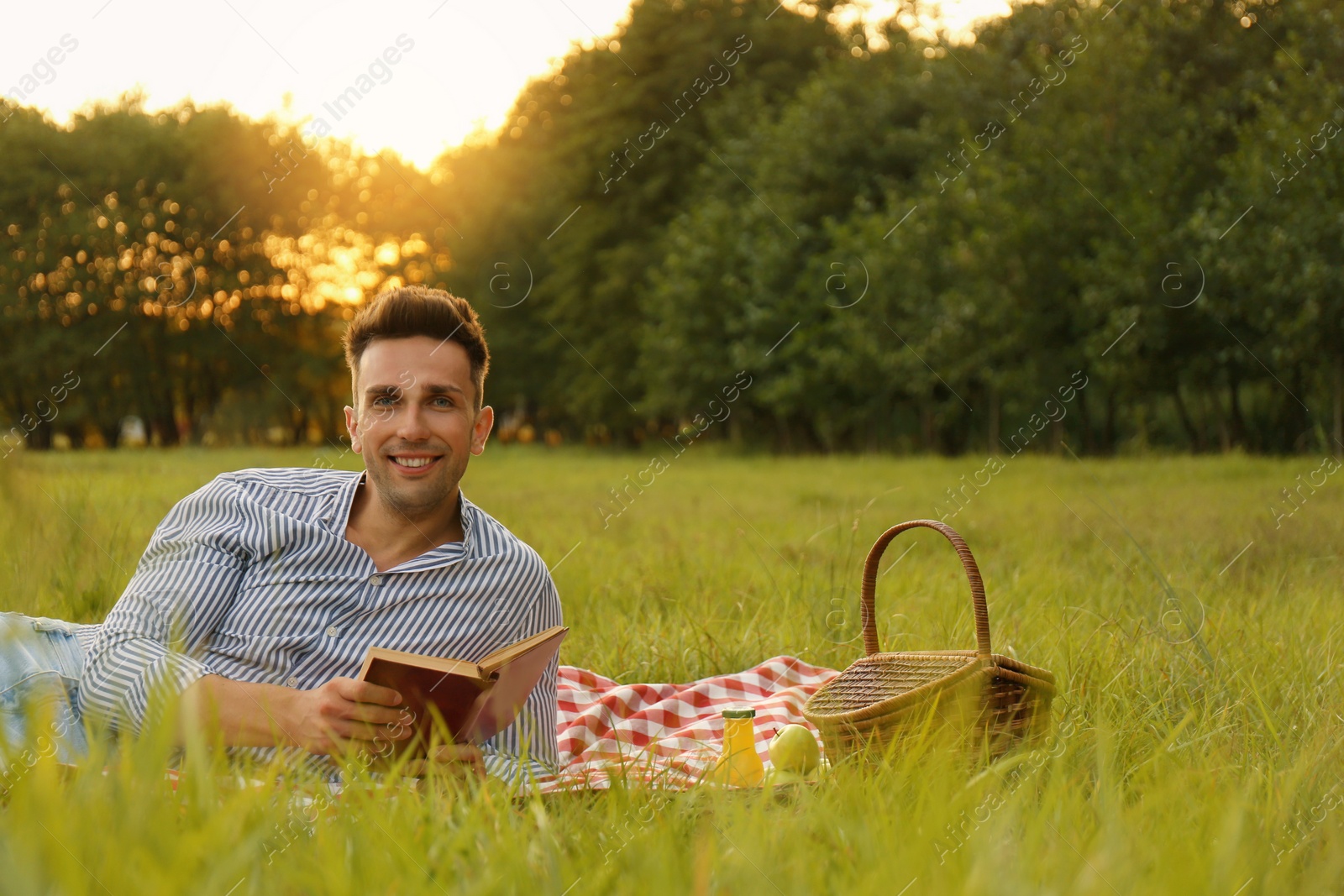 Photo of Young man reading book on picnic blanket in park