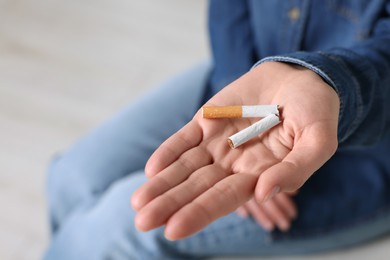 Quitting smoking concept. Woman holding broken cigarette on blurred background, closeup. Space for text