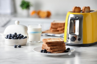 Photo of Yellow toaster with roasted bread slices, blueberries and glass of milk on white marble table