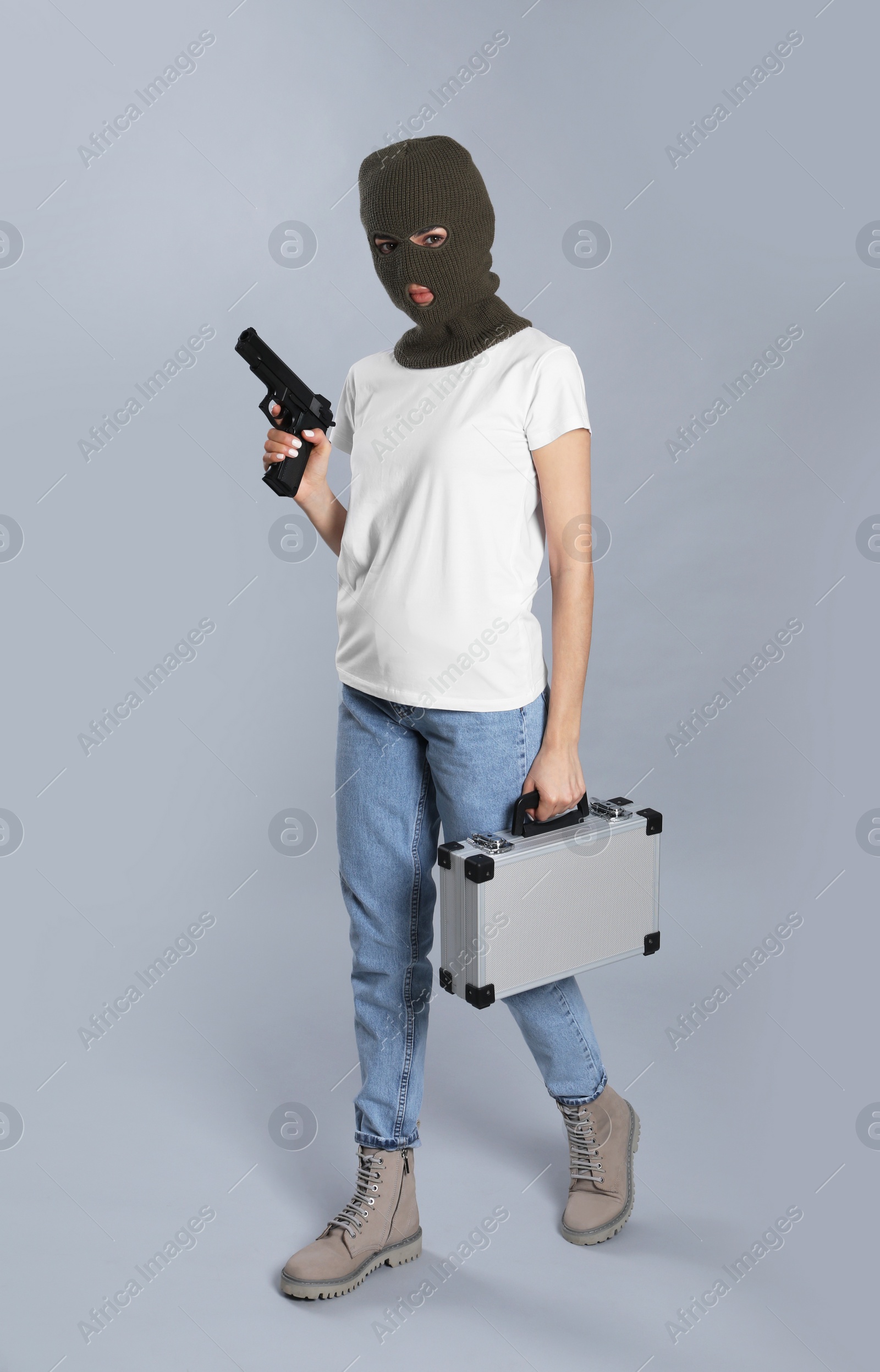 Photo of Woman wearing knitted balaclava with metal briefcase gun on grey background