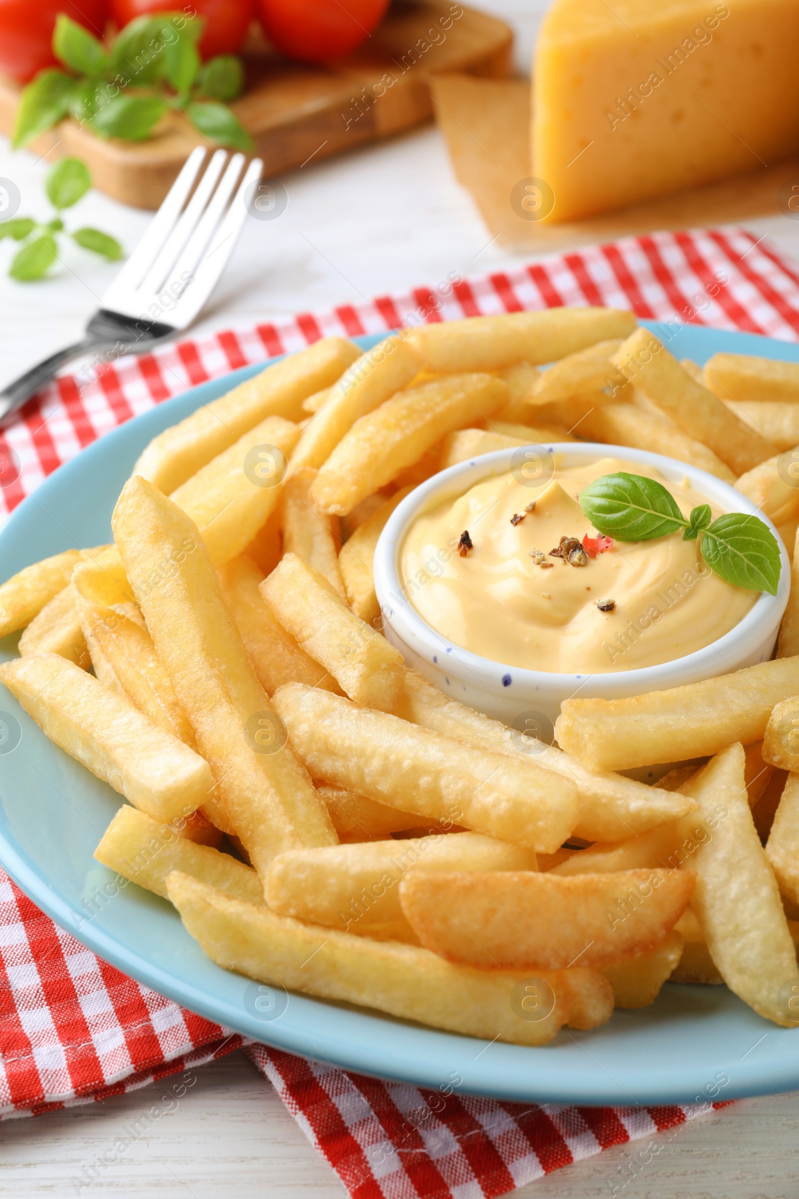 Photo of Delicious French fries and cheese sauce with basil on white table, closeup