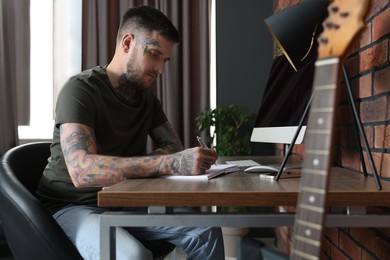 Hipster man writing near computer at wooden table in room