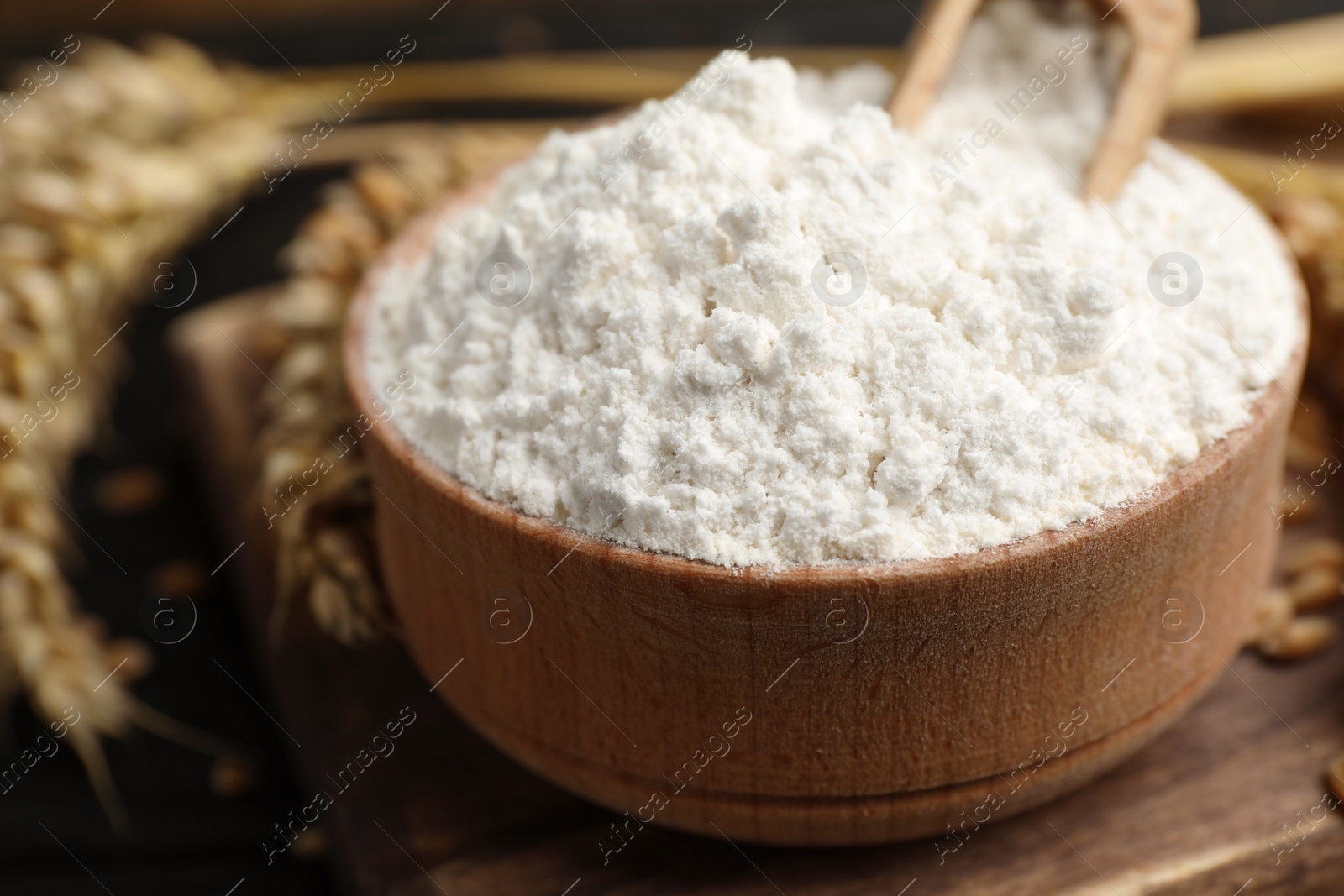 Photo of Wheat flour in bowl, spikes and grains on wooden board, closeup