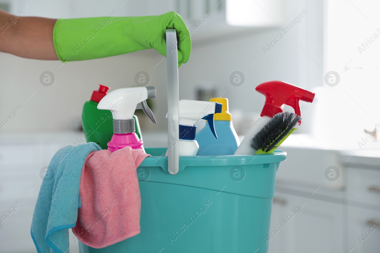 Photo of Woman holding bucket with cleaning supplies in kitchen, closeup